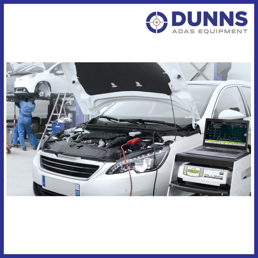 GYS GYSFLASH 100.12 HF battery support unit in use in a professional workshop, connected to a vehicle battery during diagnostic phase alongside a laptop